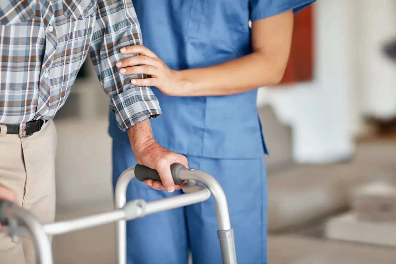 A caregiver assisting an elderly man who is using a walker.