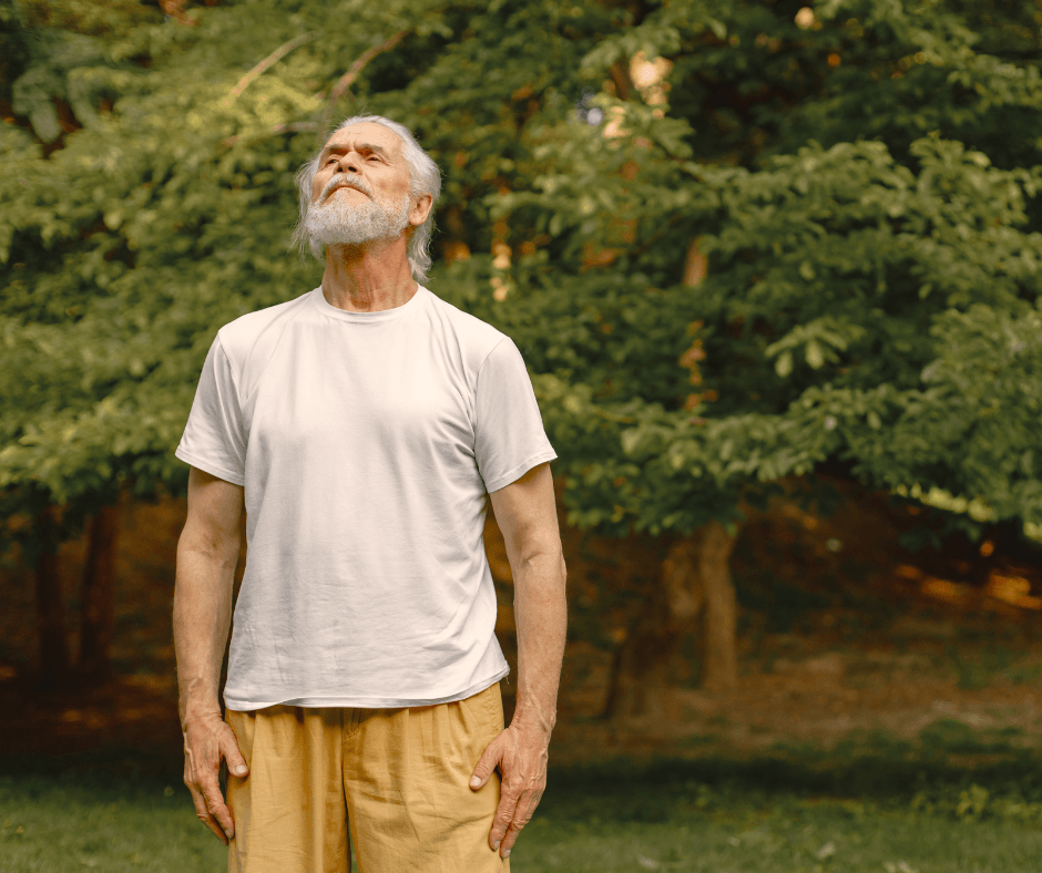Elderly man doing breathing exercises in a tranquil outdoor environment.